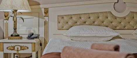 Una cama bien hecha con sábanas blancas, un cabecero color beige y una lámpara de noche.