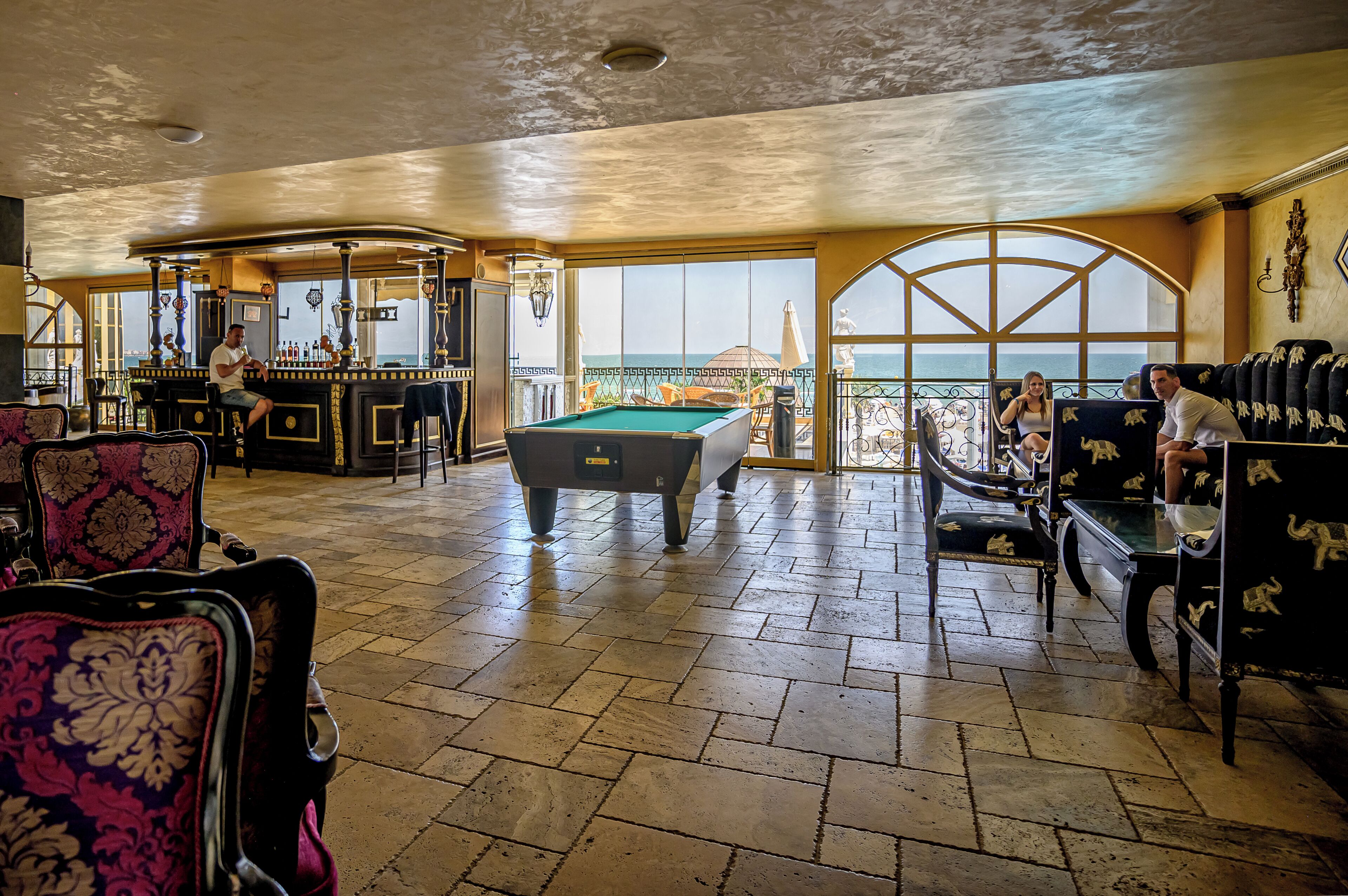 A spacious indoor area with a pool table, seating arrangements, and a view of the sea through large windows.