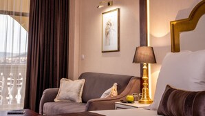 Une chambre d’hôtel avec un lit, un canapé, une lampe, un tableau au mur et une fenêtre avec des rideaux.