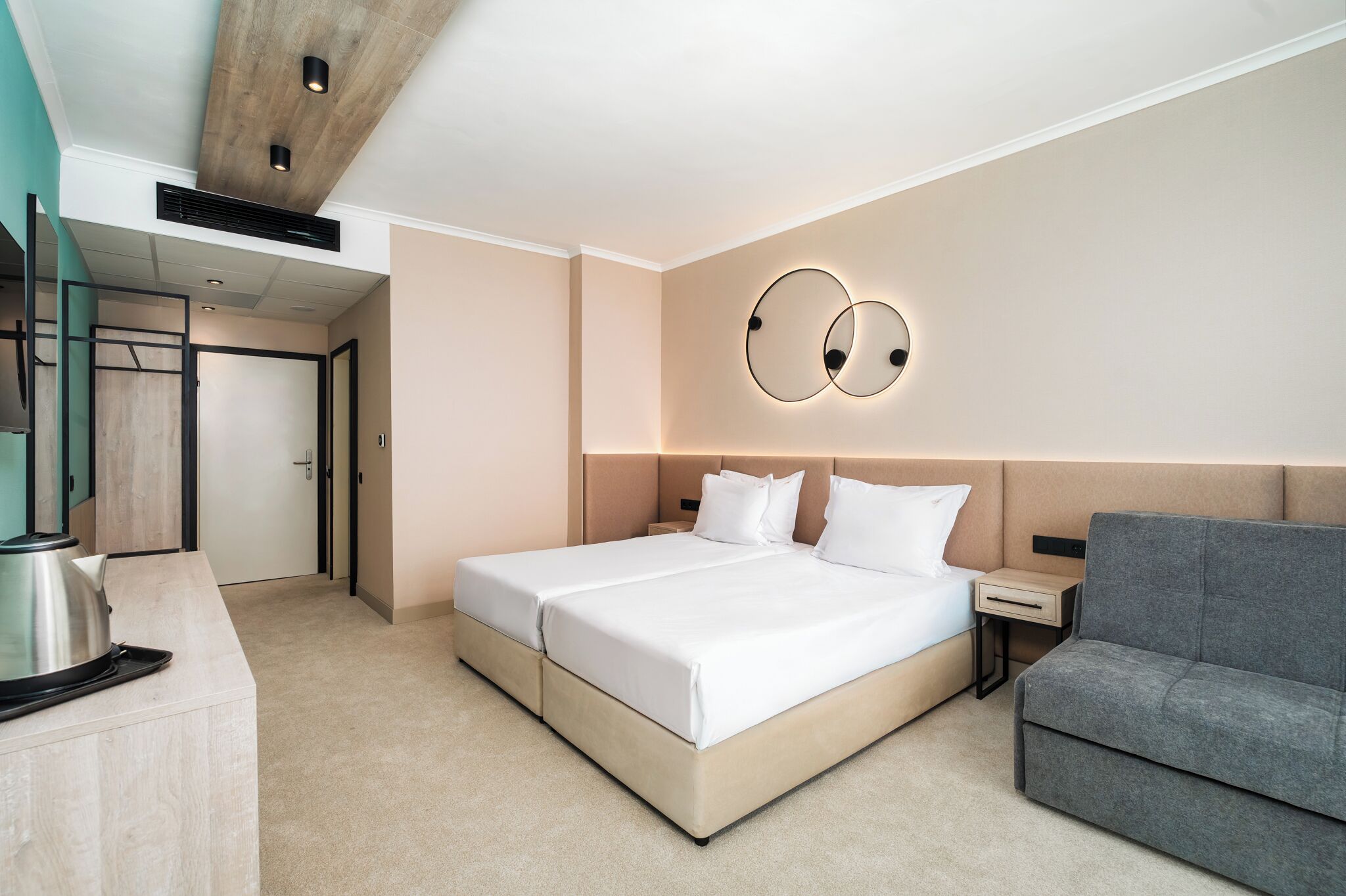 Ein modernes Hotelzimmer mit einem großen Bett, einem grauen Sofa, einem Nachttisch und einer wandmontierten Lampe.