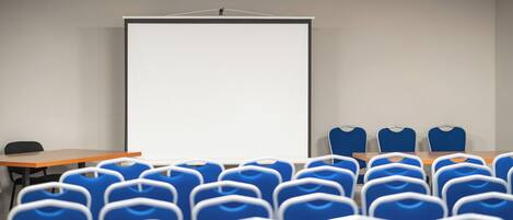 Una sala conferenze con uno schermo bianco grande, sedie blu e un tavolo di legno.