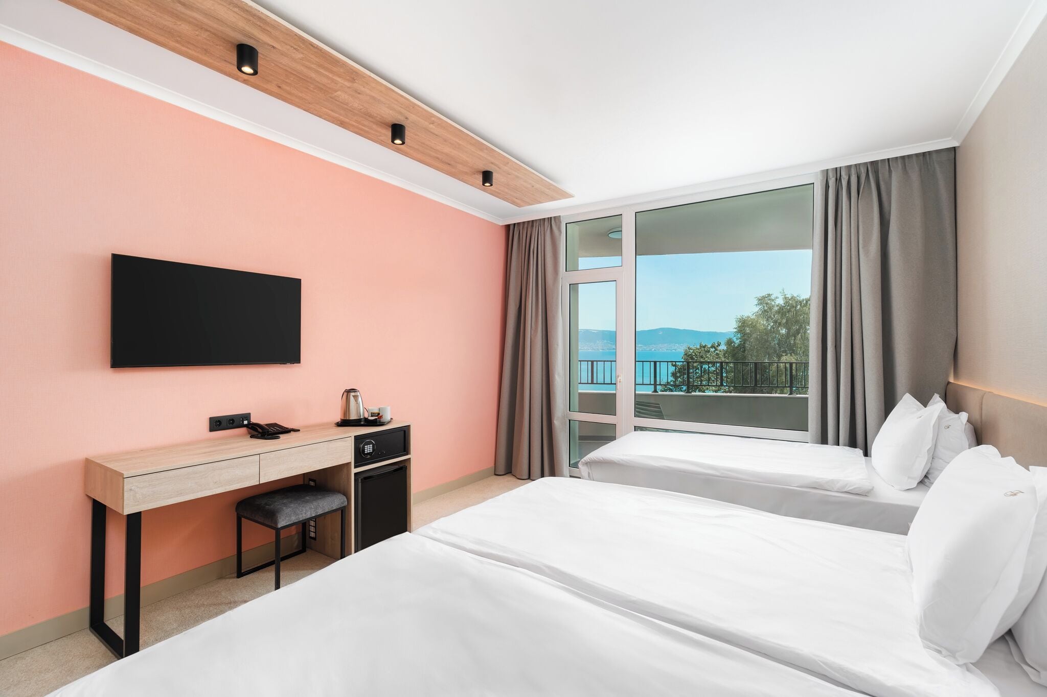 Ein Hotelzimmer mit Schreibtisch, zwei Betten, Fernseher und Blick ins Freie.