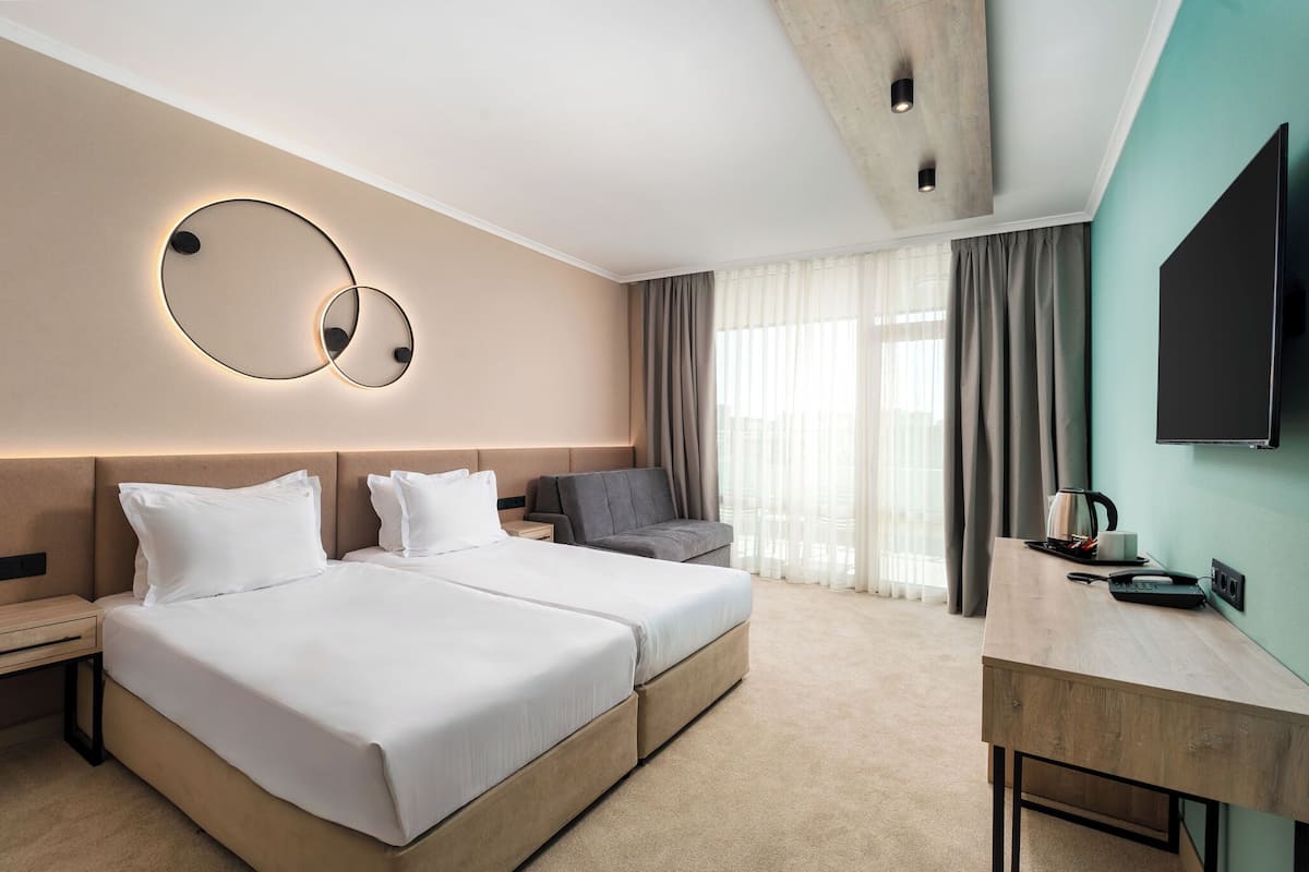A hotel room with a double bed, a desk, a chair, a TV, and a wall-mounted light fixture.