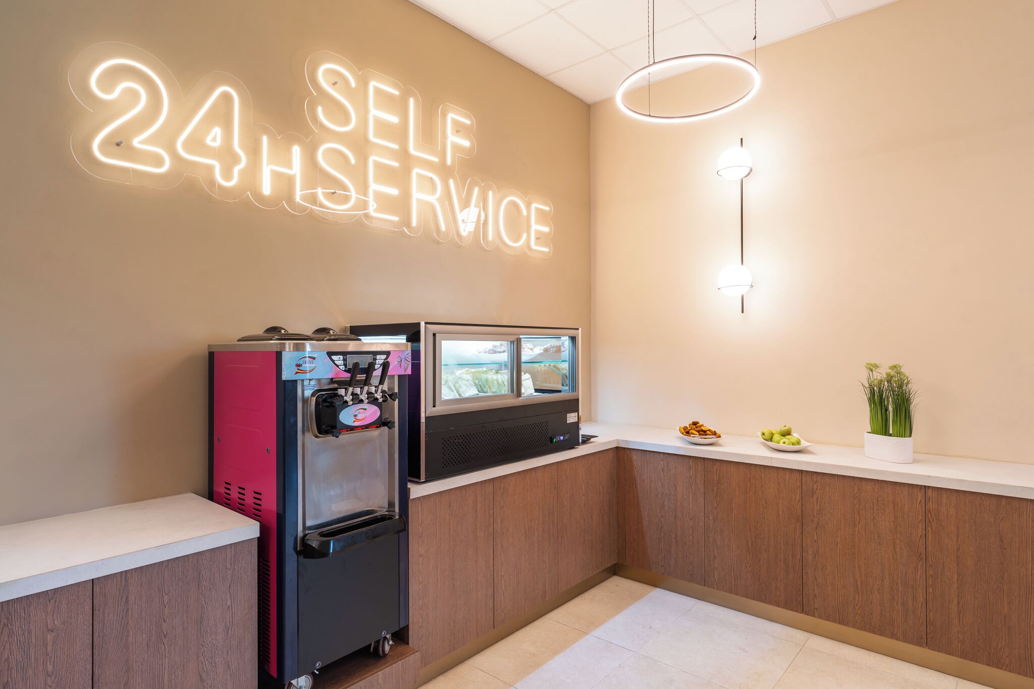 Un espace équipé de bornes en libre-service, avec un panneau lumineux au néon, un distributeur d’eau et une petite plante posée sur le comptoir.