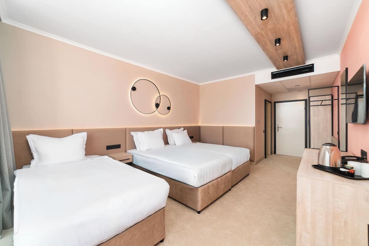 A hotel room with two beds, a wooden ceiling, a TV, and a kitchenette.