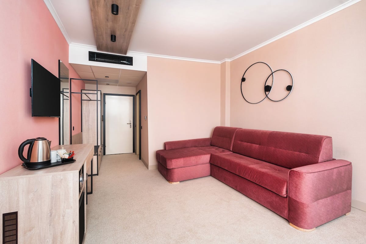 A modern room with a pink wall, a red sectional sofa, a flat-screen TV, and a wooden ceiling.