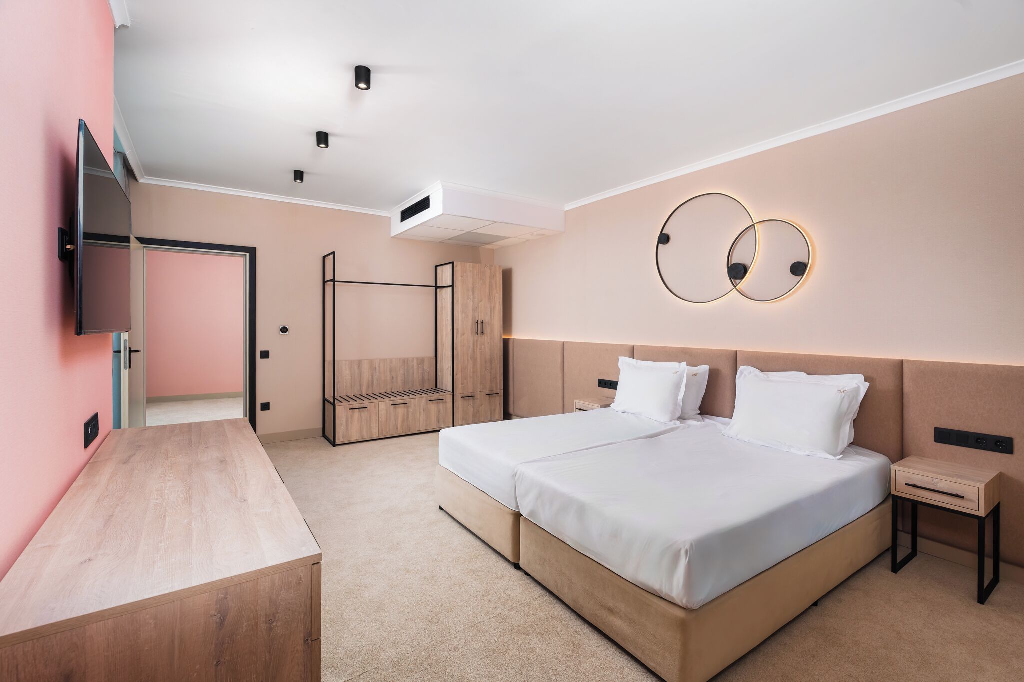 Een moderne hotelkamer met een groot bed, een houten nachtkastje, een flatscreen televisie aan de muur en een plafondlamp.
