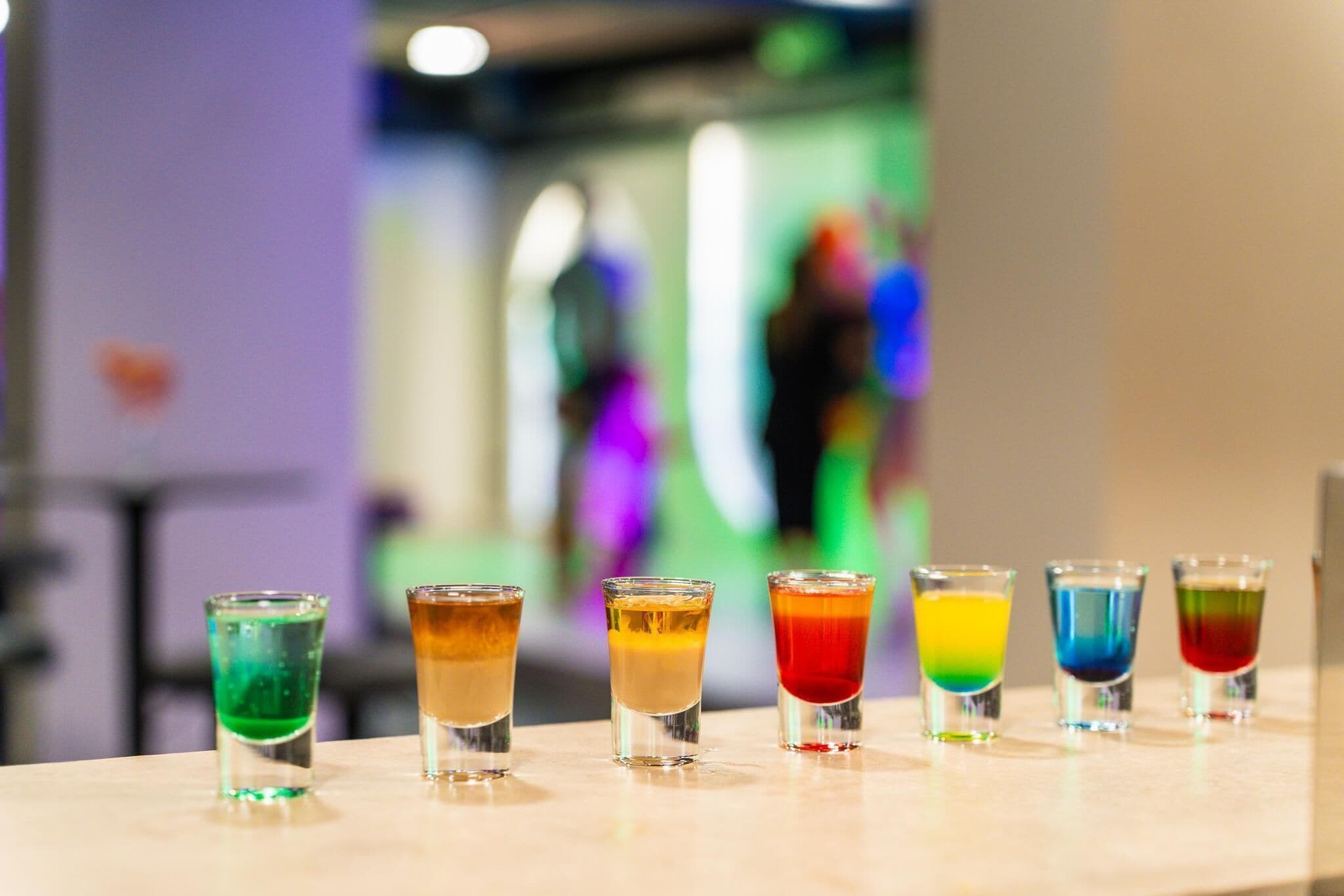 A row of colorful shot glasses on a bar counter.