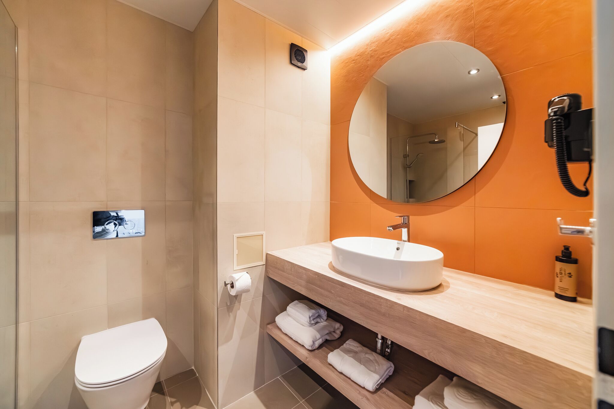 Une salle de bain moderne avec des toilettes blanches, un miroir rond et un lavabo avec un meuble-vasque en bois.