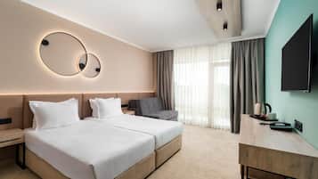 Habitación de hotel con cama doble, escritorio, silla, televisor y ventana grande con cortinas.