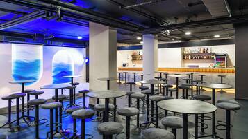 A bar area with multiple stools and tables, a bar counter with bottles, and a wall with a blue light display.