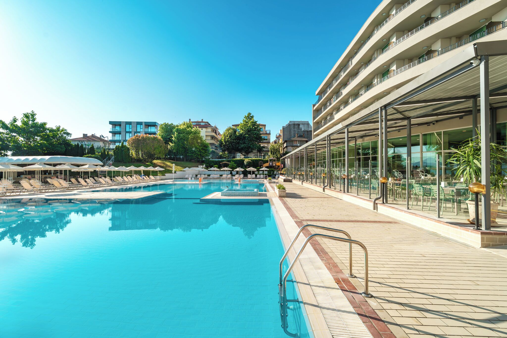 En swimmingpool med liggestole og en terrasse med glas, der har udendørs siddepladser.