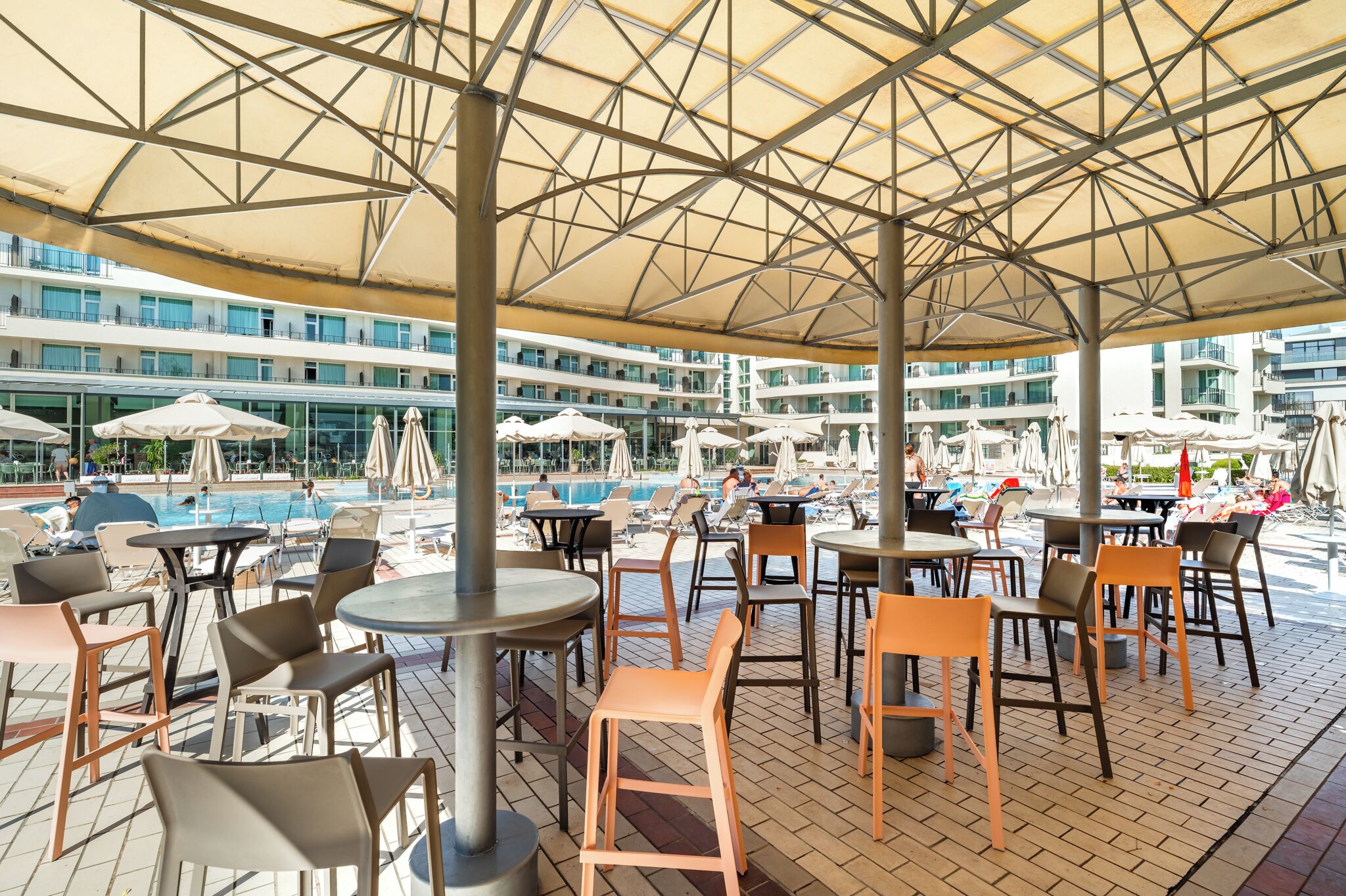 Un bar en la azotea con mesas al aire libre, piscina y vistas a un edificio moderno.