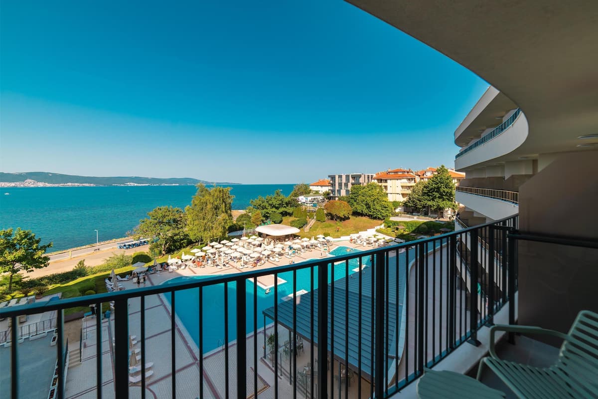 A balcony with a view of a pool, beach, and sea.