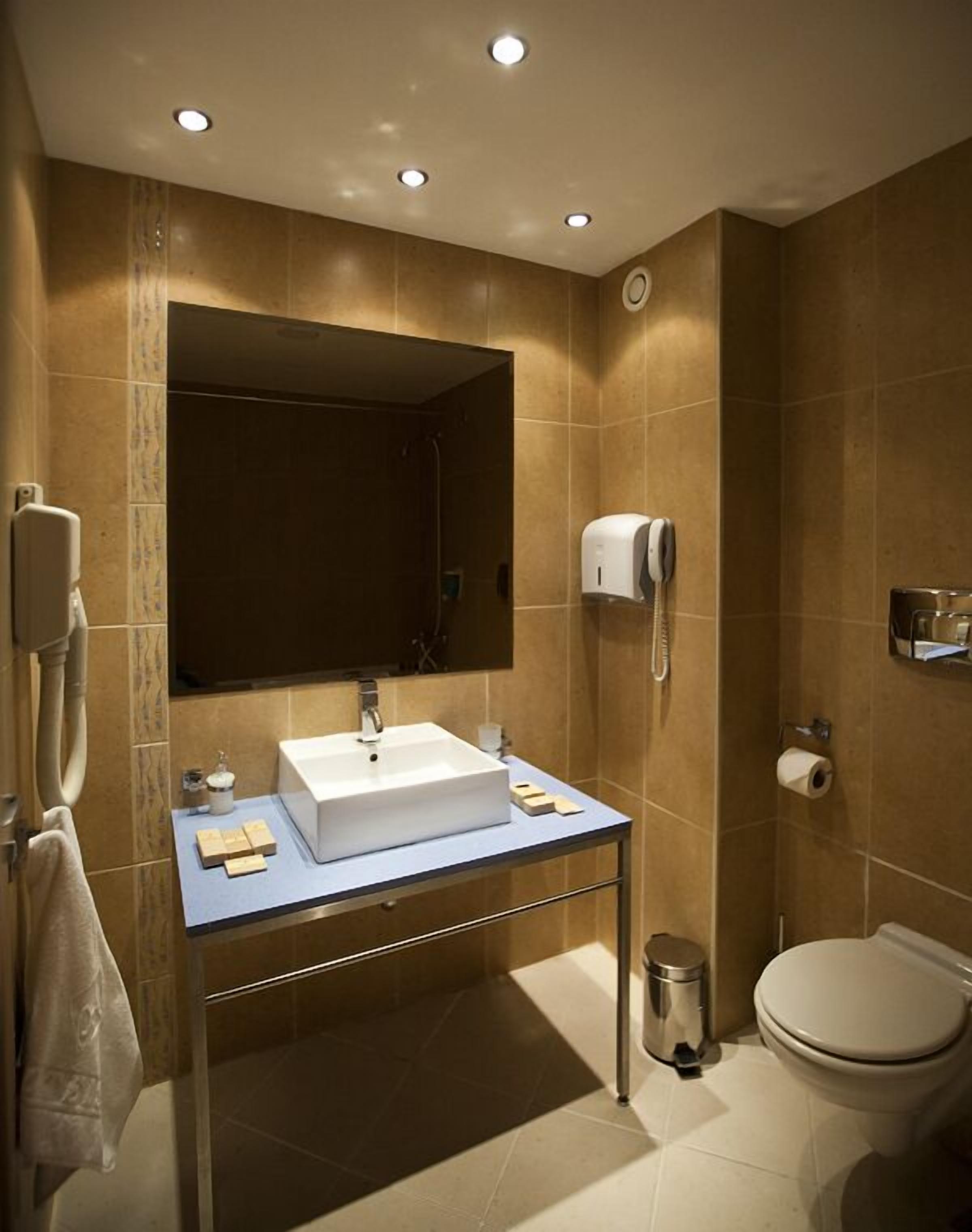 A modern bathroom with a large mirror, a sink, a toilet, and a hand dryer.