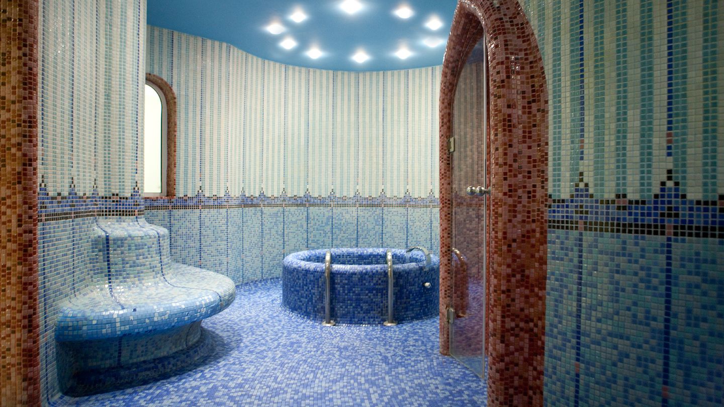 A bathroom with mosaic tile walls, a blue-tiled floor, and a circular blue bathtub.