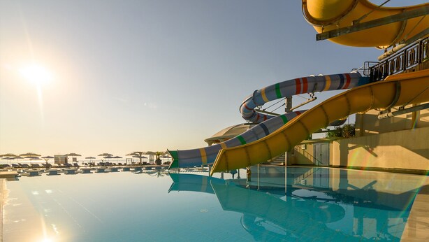 A swimming pool with a water slide, lounge chairs, and umbrellas. - Azalia Hotel Balneo & SPA (Varna)