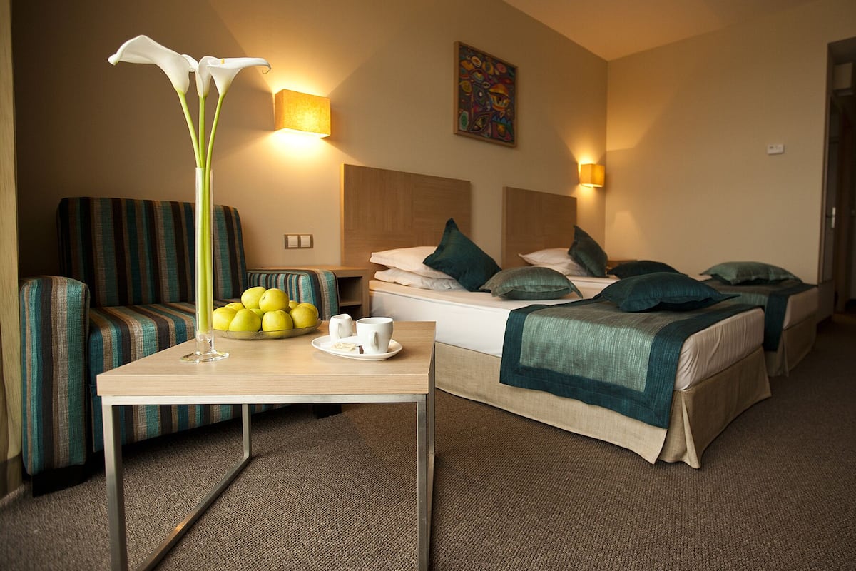 A hotel room with a bed, a bedside table with a vase of flowers, a bowl of fruit, and a chair.
