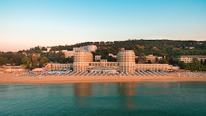 A coastal hotel with multiple buildings, a beach with rows of sun loungers, and a calm sea. - Azalia Hotel Balneo & SPA (Varna)