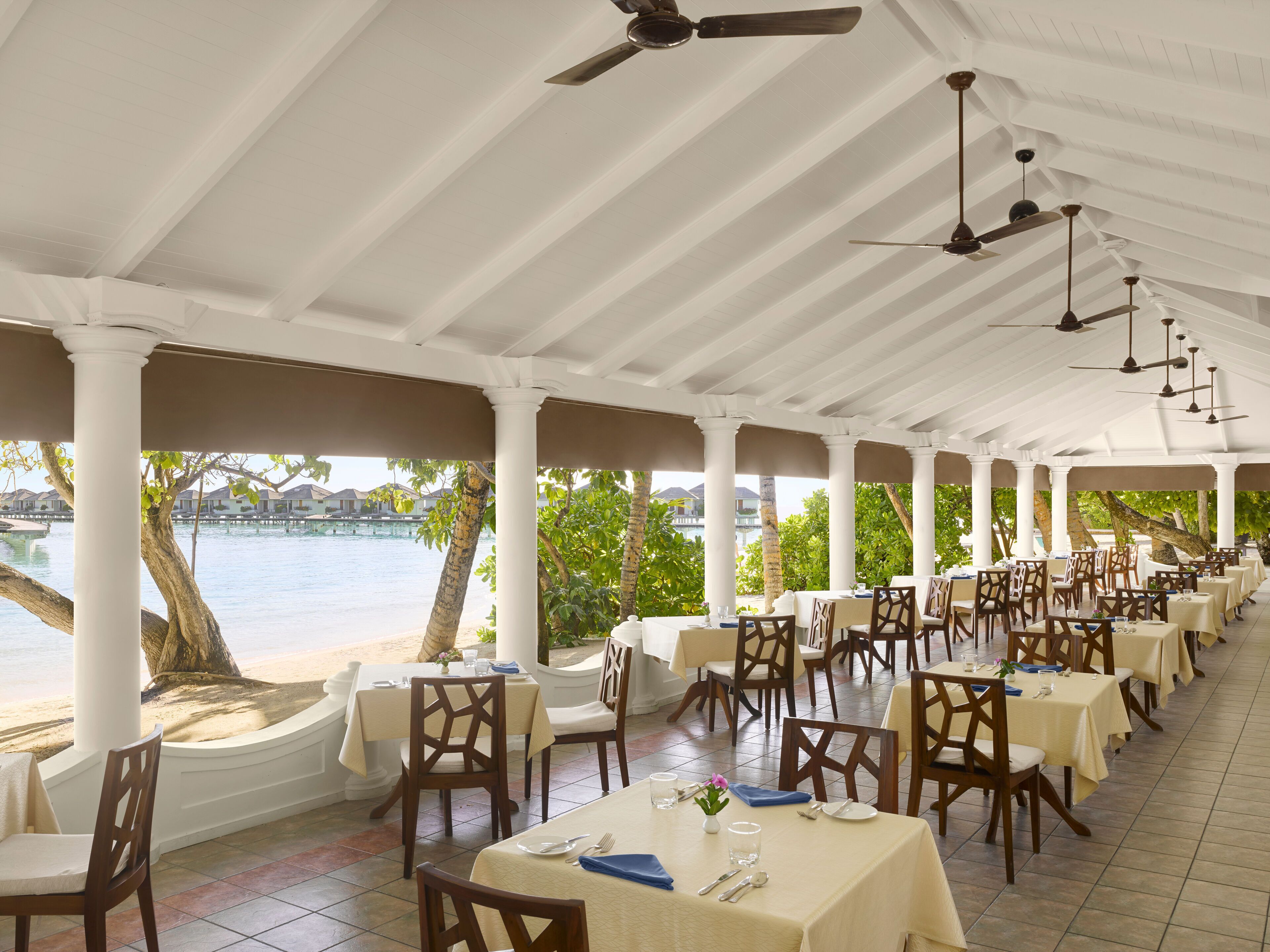 A covered outdoor dining area with tables and chairs, overlooking a body of water.