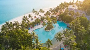 Vista aérea de un resort con piscina rodeada de palmeras y una playa.