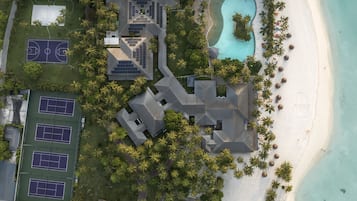 Vista aérea de un resort con piscina, canchas de tenis y palmeras.