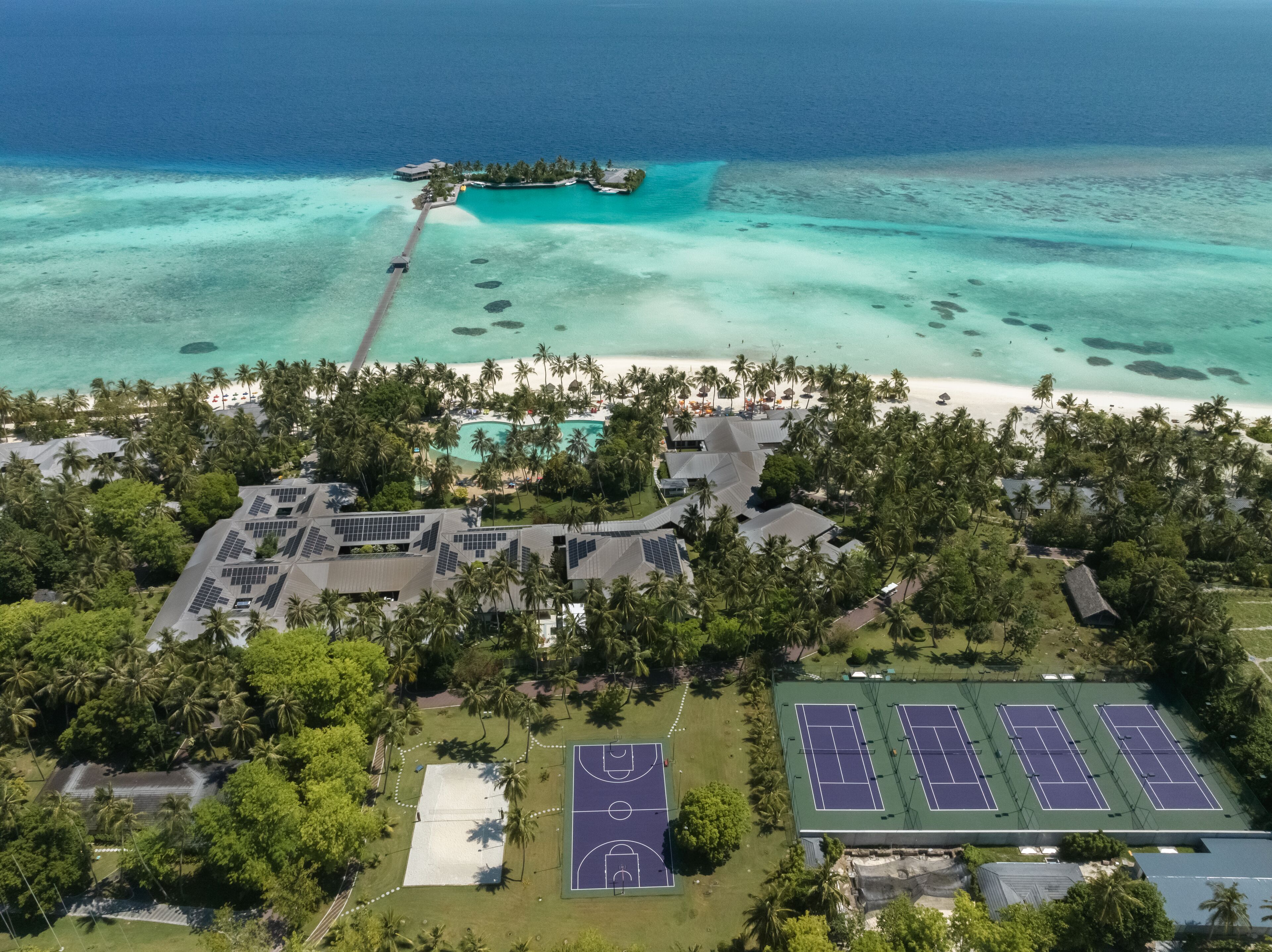 An aerial view of a resort with a beach, a small island, and tennis courts.