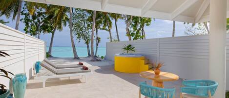 A covered outdoor area with a pool, lounge chairs, and a table with chairs.