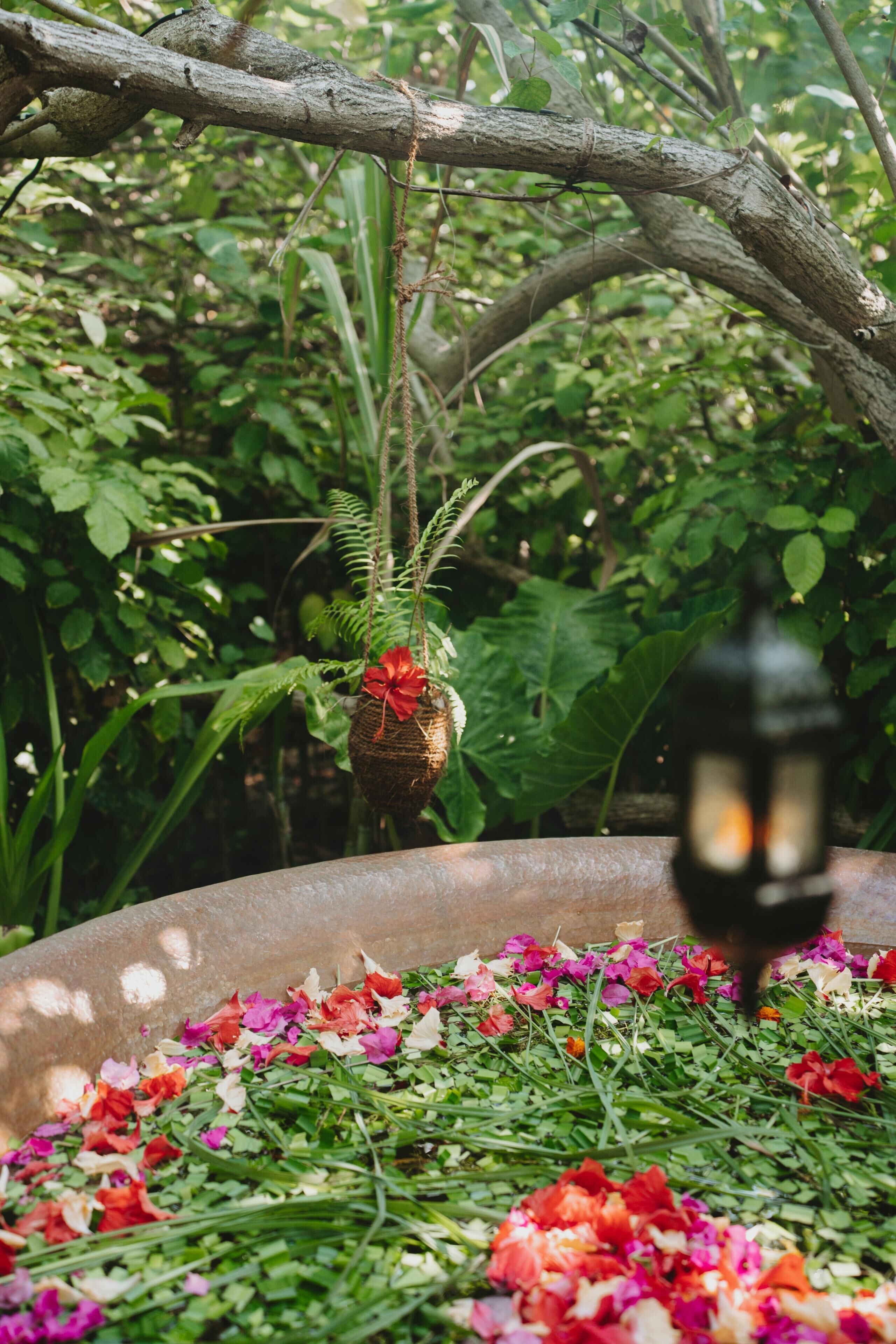 A garden with a decorative hanging ornament, a lantern, and a flower-filled planter.