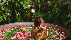 A woman sitting in a bathtub filled with flowers, surrounded by greenery and hanging lanterns.