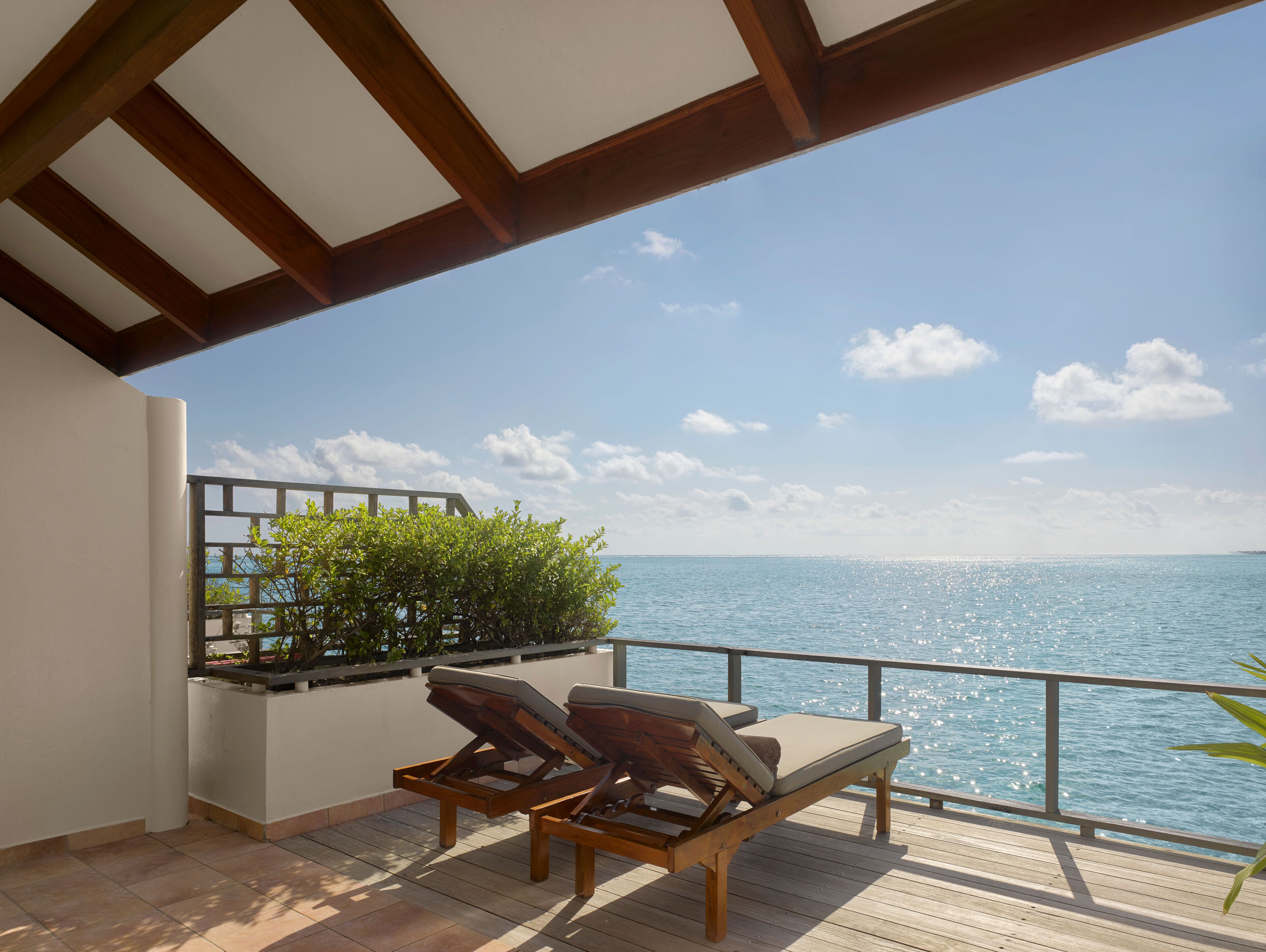 A wooden deck with two lounge chairs facing a clear blue sea.