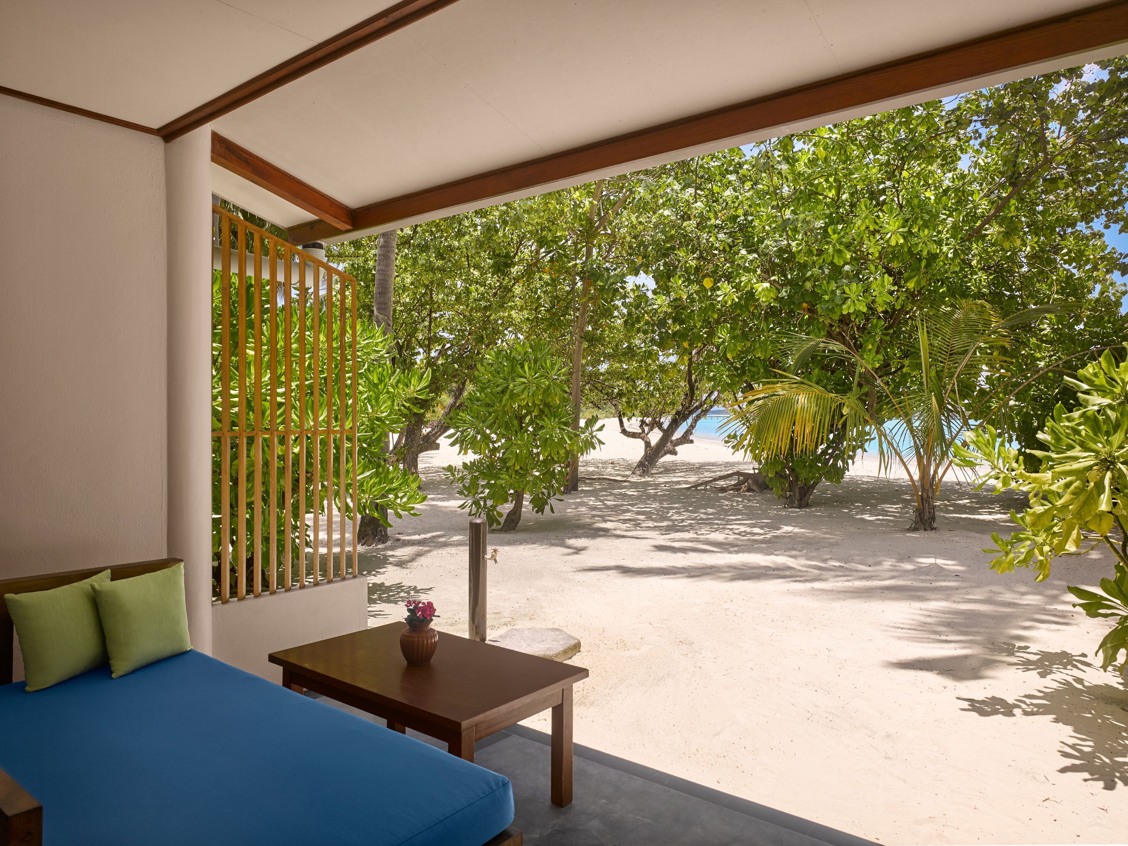 A room with a bed, a small table, and a view of a beach with trees.