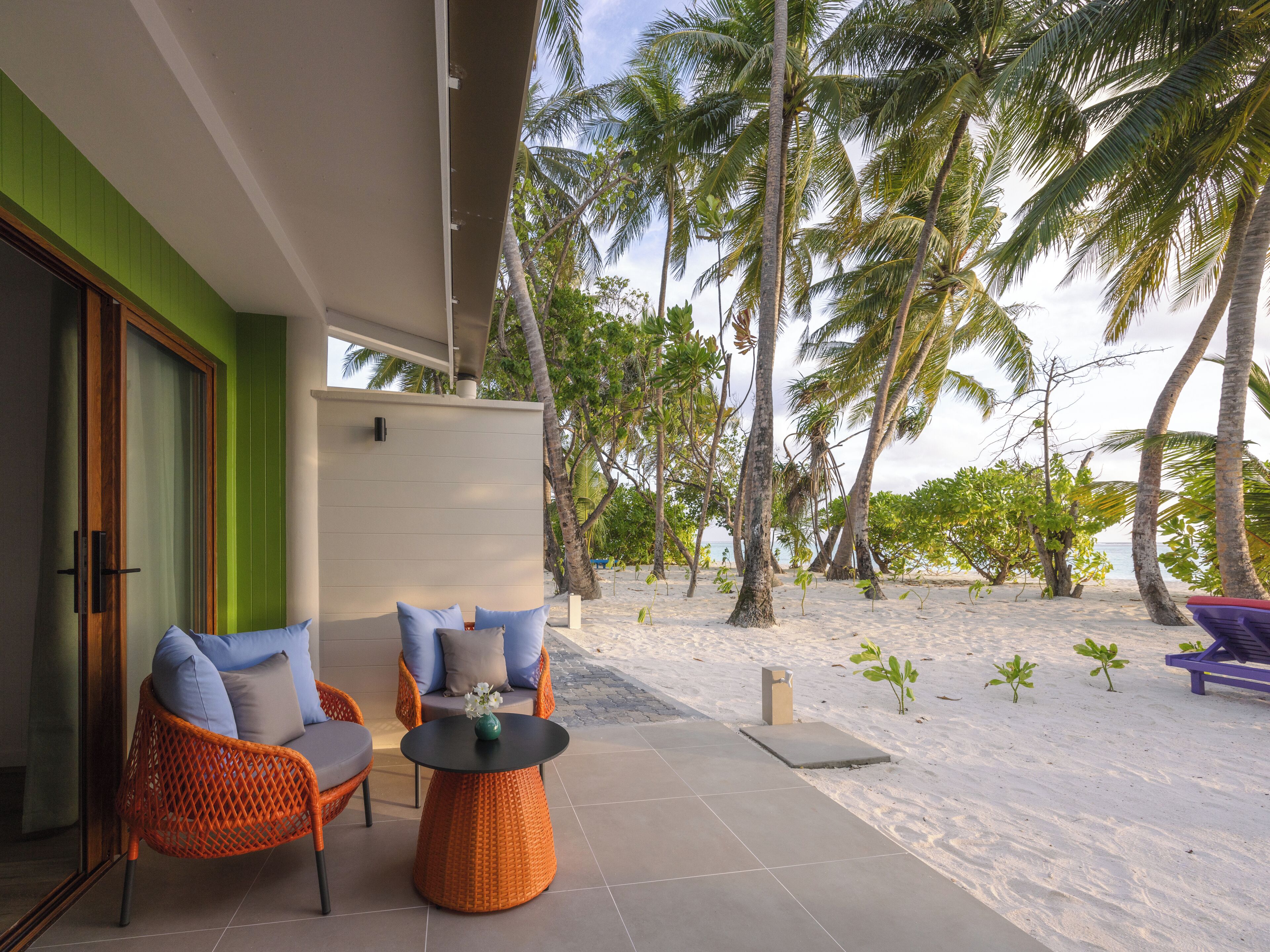 A beachside patio with wicker furniture, a round table, and a view of palm trees and the ocean.