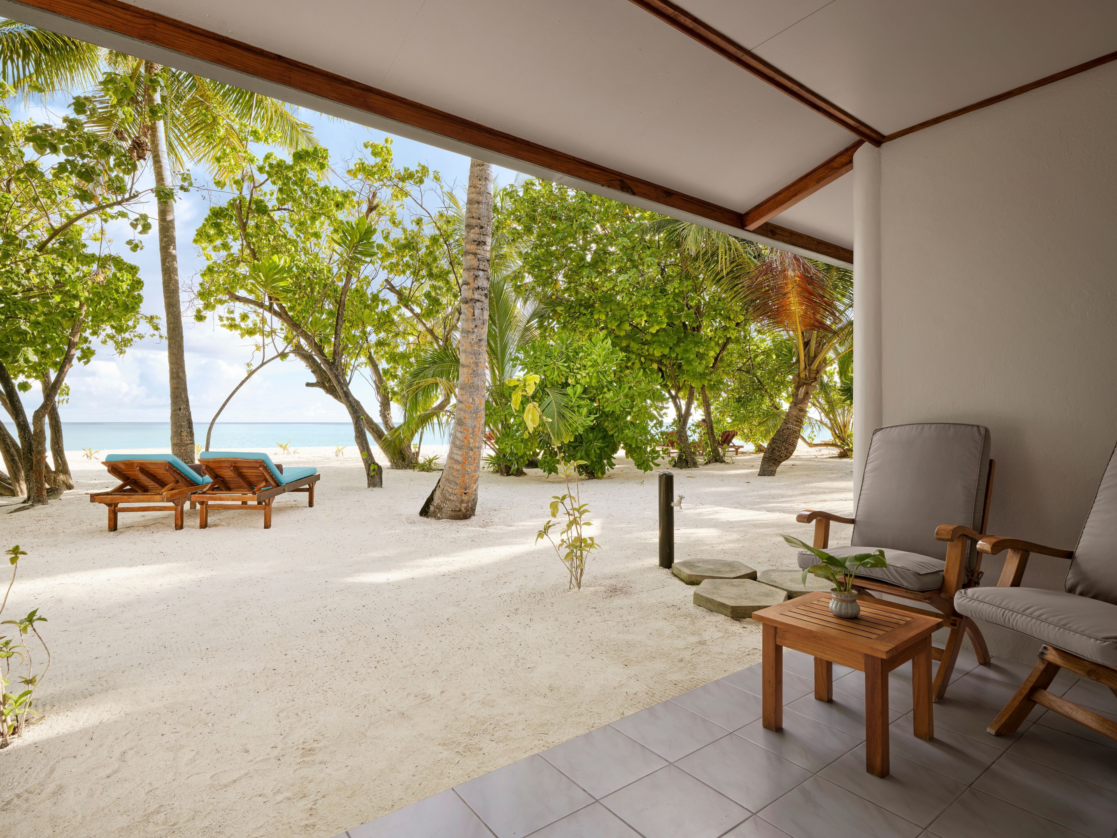 Eine Strandlounge mit Holzmöbeln, Blick auf das Meer und tropischen Bäumen.