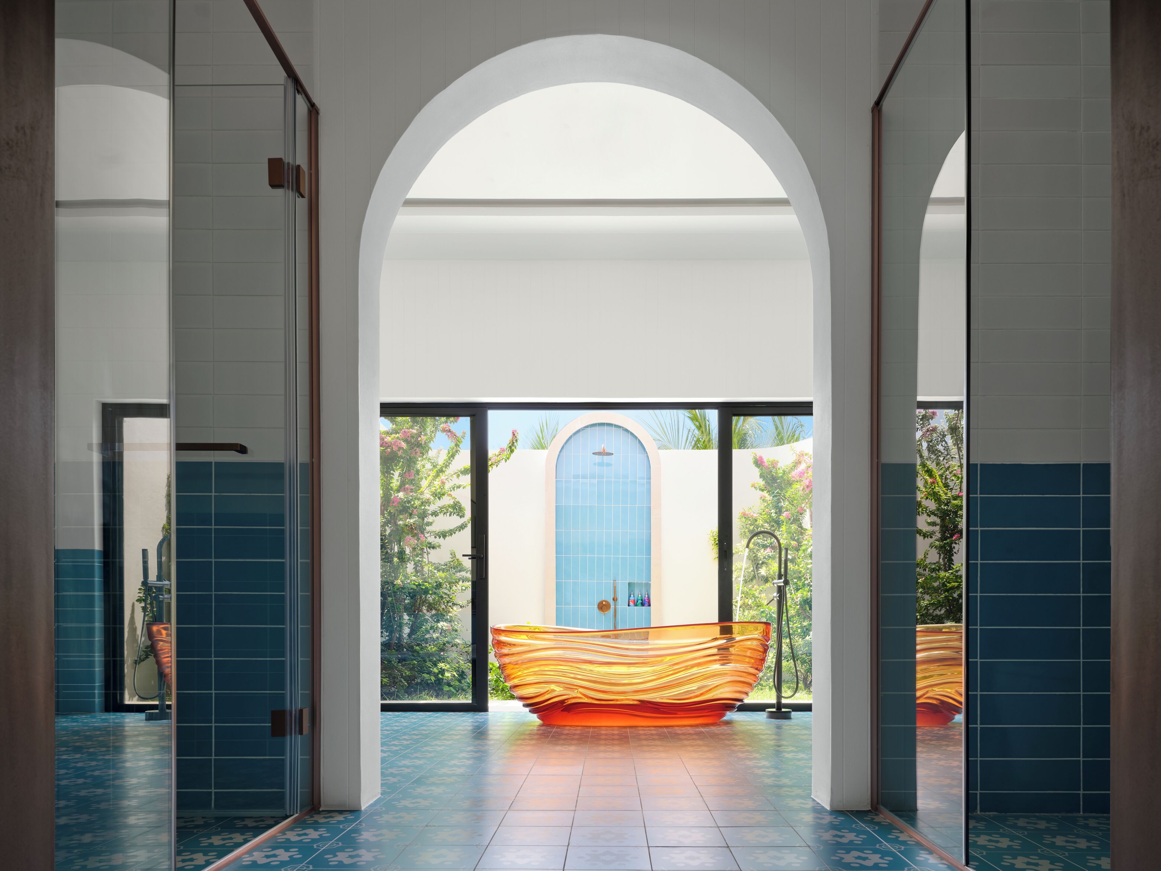 A hallway with a large arched doorway leading to a room with a blue-tiled wall and a large orange object in the center.