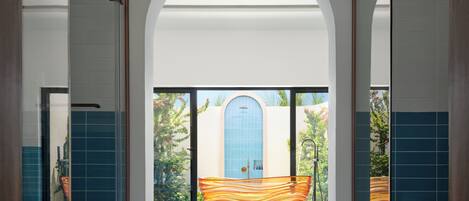 Ein Flur mit einem großen Bogenportal, das in einen Raum führt, dessen Wand blau gefliest ist und in dem sich mittig ein großes orangefarbenes Objekt befindet.