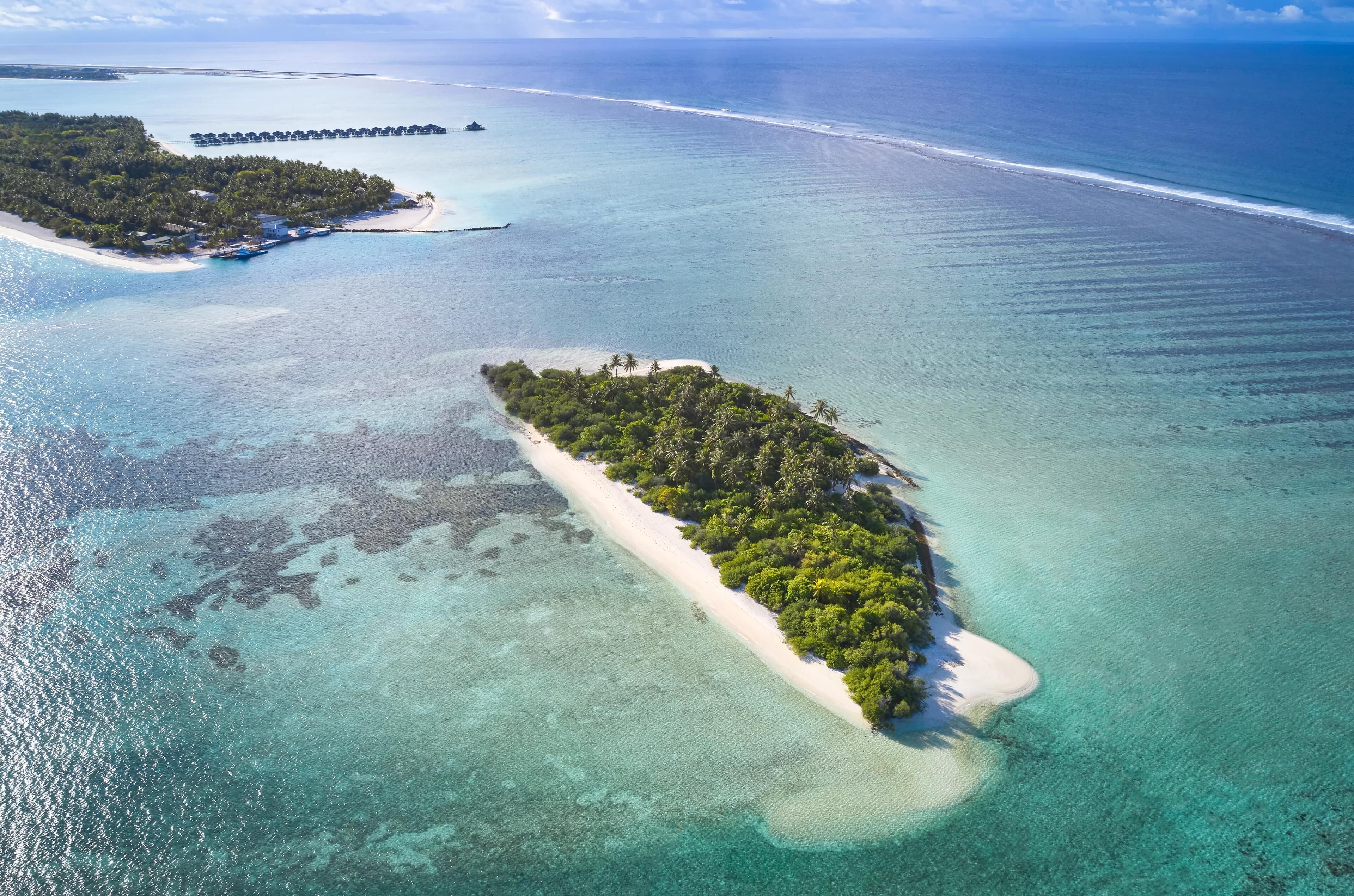 An aerial view of a tropical island with clear turquoise waters, a sandy beach, and dense greenery.