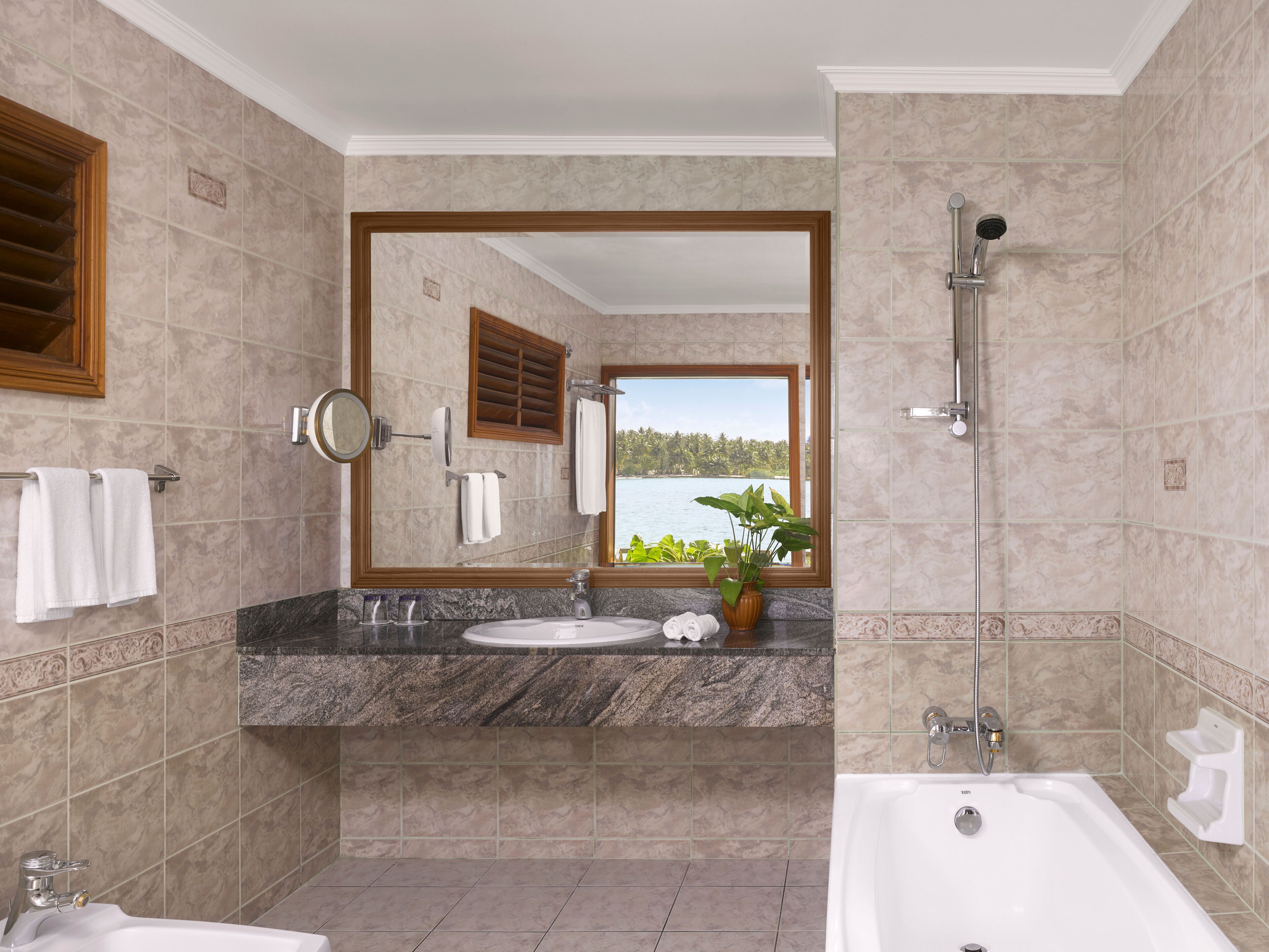 A bathroom with a marble countertop, a sink, a mirror, a shower, and a view of a lake through a window.