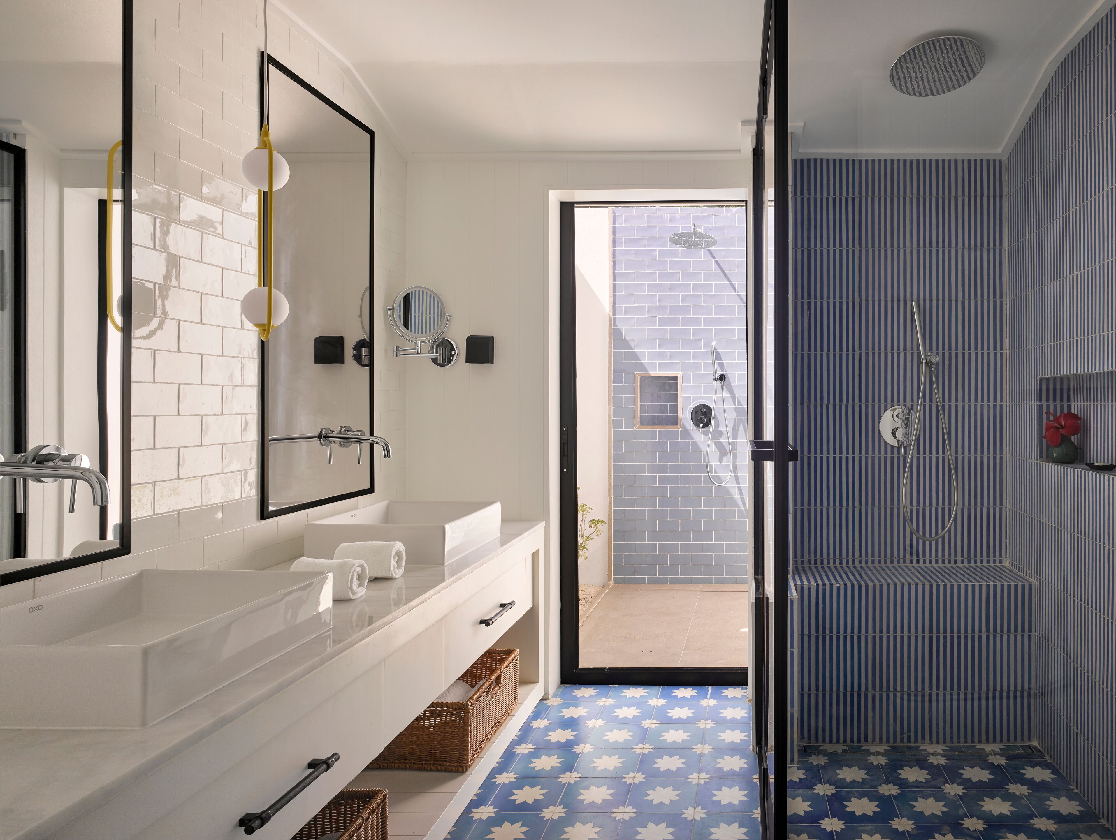 Une salle de bain moderne avec un grand miroir, un meuble-lavabo blanc et un espace douche aux carreaux rayés.