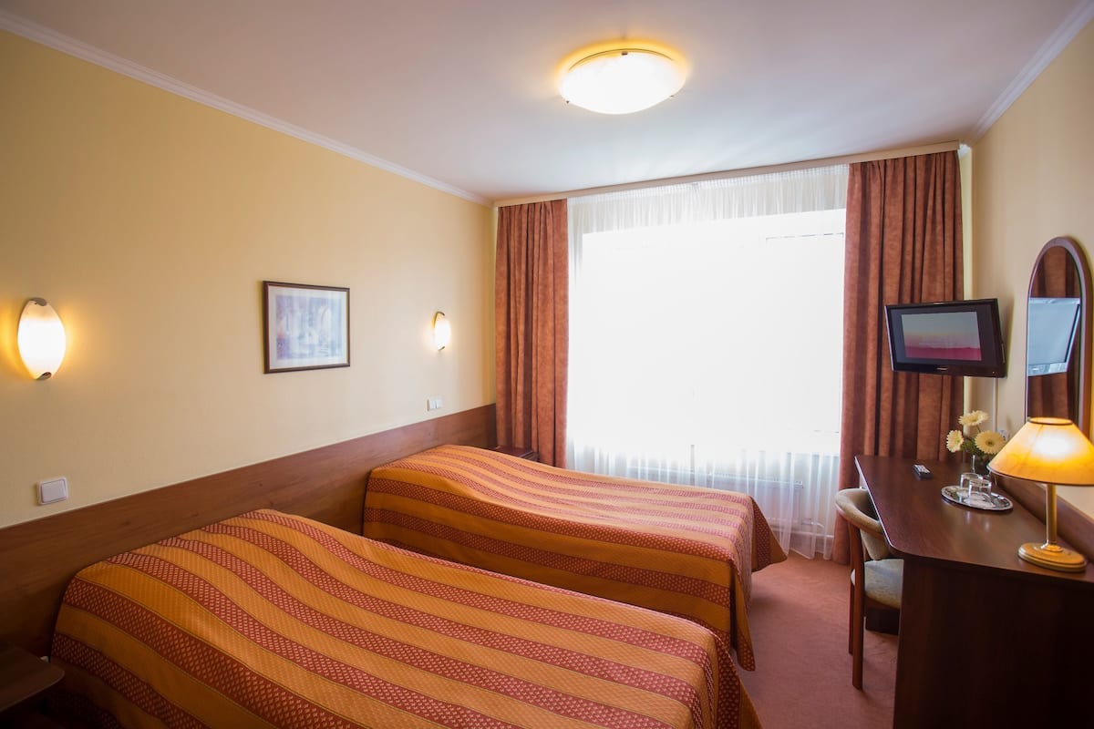 Habitación de hotel con dos camas, un escritorio con lámpara, un televisor y una ventana con cortinas.