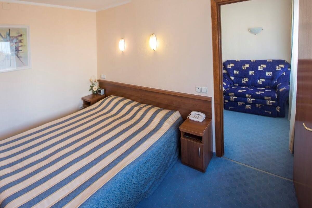 Habitación de hotel con cama, mesita de noche y espejo que refleja un sofá azul.