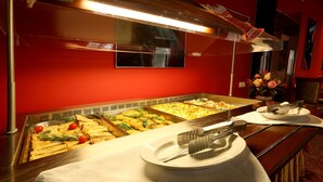 A buffet setup with various dishes, a knife and fork on a plate, and a vase with flowers. - Sputnik (Minsk)