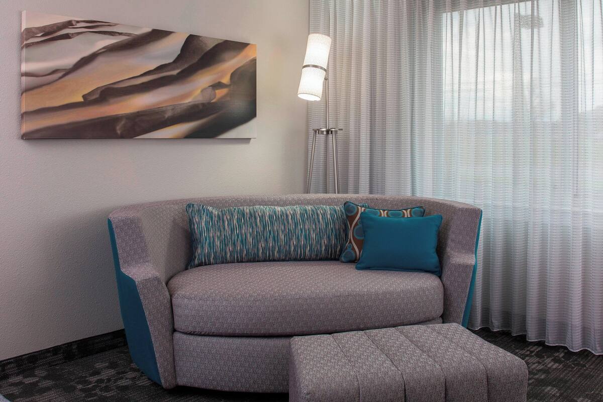 Un salon moderne avec un canapé gris, des coussins turquoise, une lampe sur pied et un grand tableau abstrait accroché au mur.