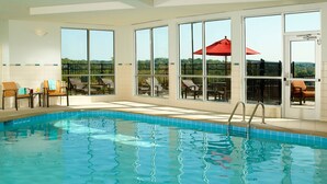 An indoor swimming pool with clear blue water, large windows, and outdoor seating with umbrellas. - Courtyard by Marriott Nashville Goodlettsville (Goodlettsville)
