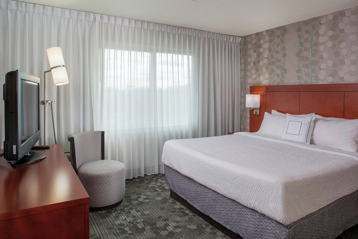 A hotel room with a large bed, a desk with a computer, a chair, and a lamp.