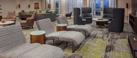 Un'ampia hall d'hotel con diverse zone relax, tra cui divani e poltrone, disposte attorno a un tavolino da caffè.