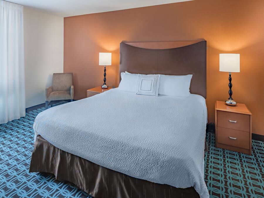 Ein Hotelzimmer mit einem großen Bett, zwei Nachttischen mit Lampen, einem Sessel und einem Teppich mit Muster.