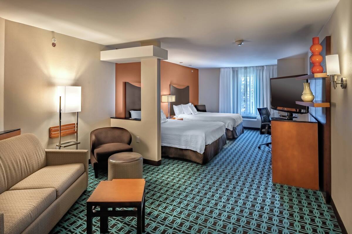 A hotel room with a sofa, two beds, a desk, a TV, and a patterned carpet.