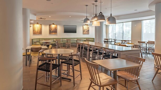 Een ruim restaurant met hoge tafels en stoelen, hangende verlichting en een groot raam dat natuurlijk licht binnenlaat.
