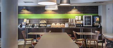 A modern restaurant with a long communal table, multiple chairs, and a counter with food and beverage dispensers.